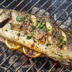 Close-up shot of perfectly cooked branzino on the grill with crispy skin, juicy flesh, and garnished with fresh herbs and lemon slices.